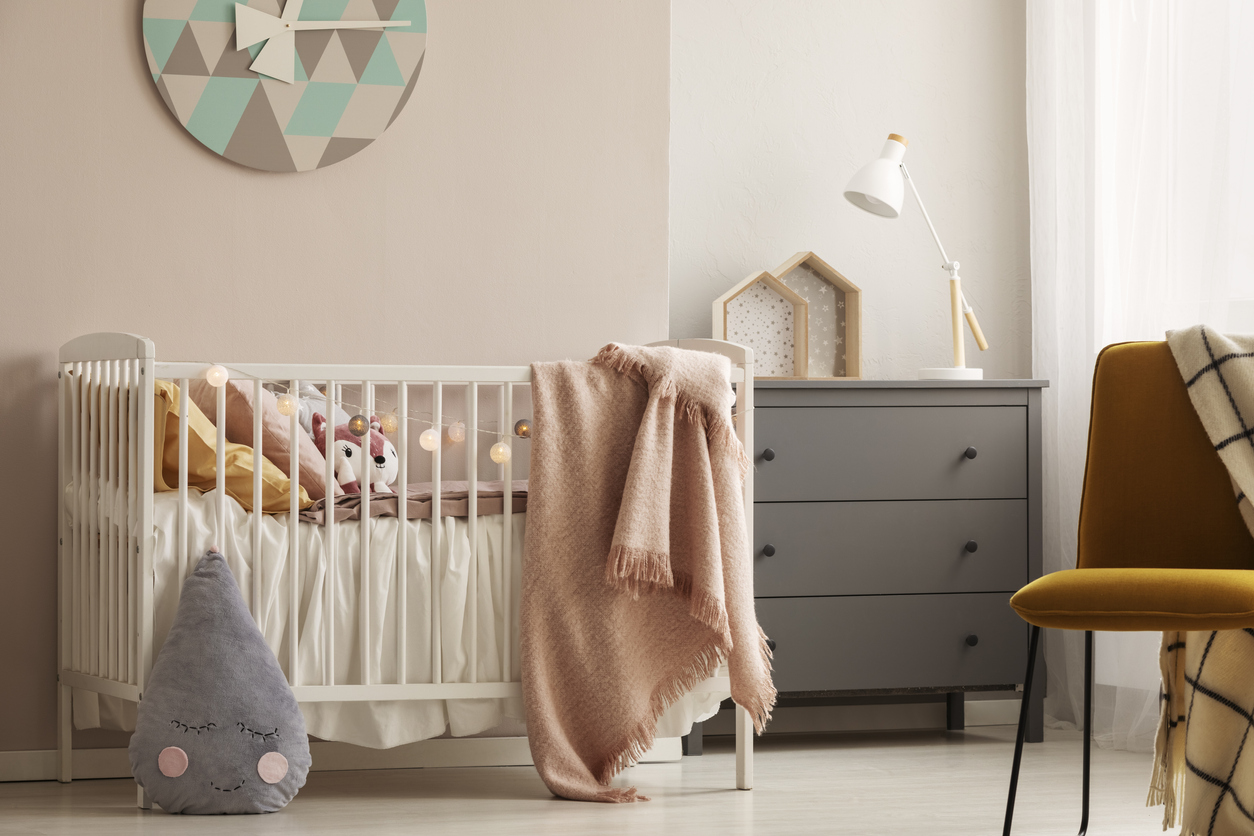 Pillows and toy in white wooden crib with pastel pink blanket in bright nursery image