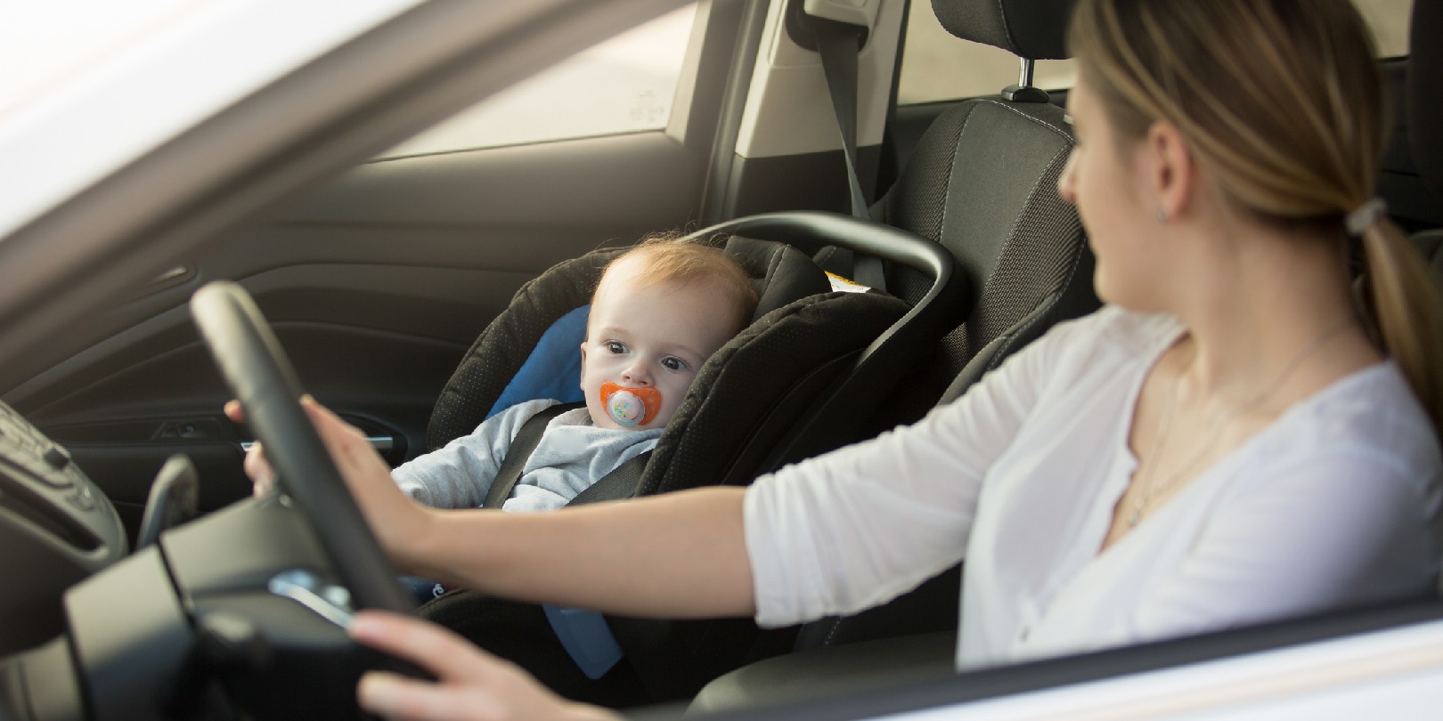 Woman driving car with baby sitting on front seat