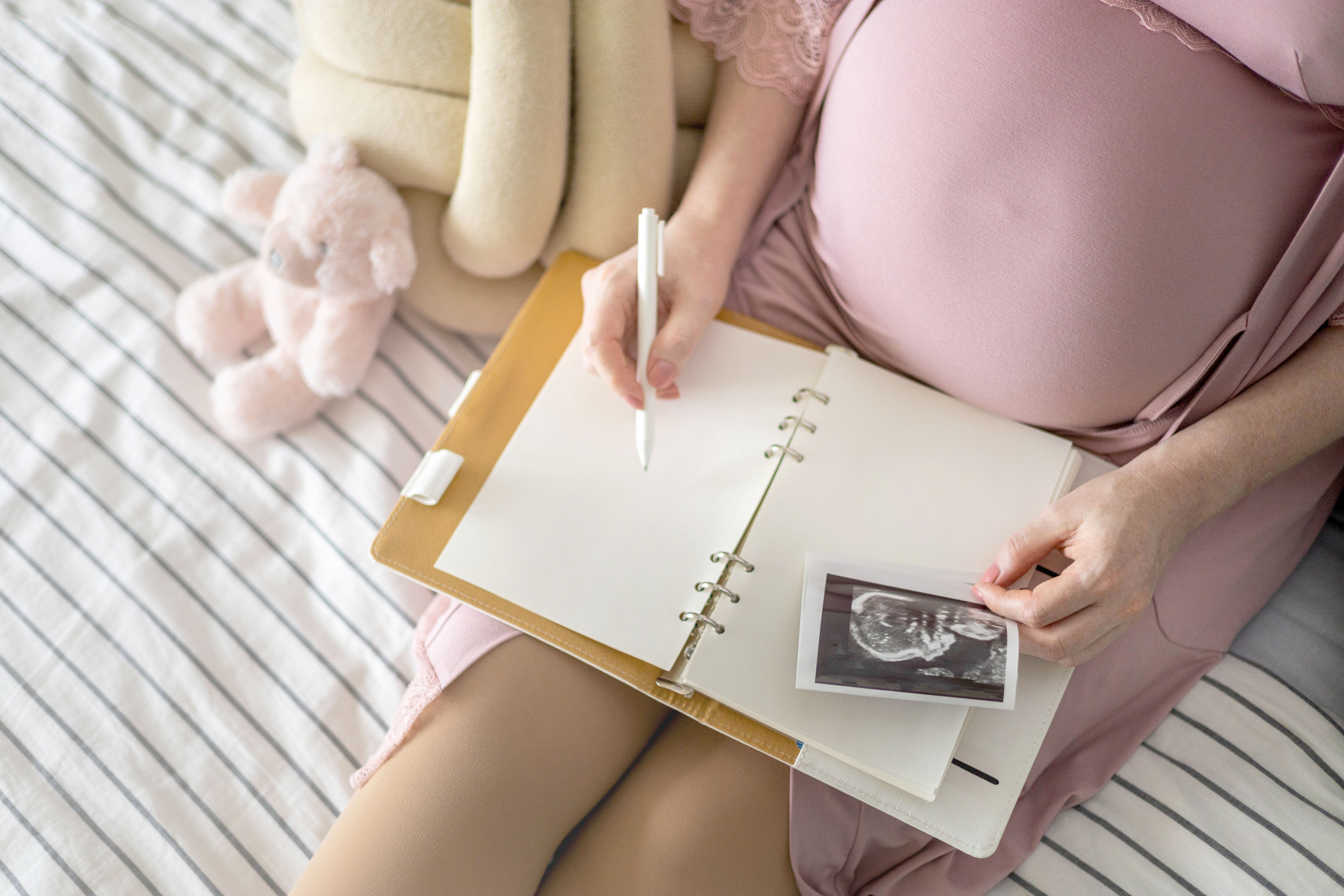 Top view caring future mother writing diary with ultrasound x ray photo sitting on comfortable bed