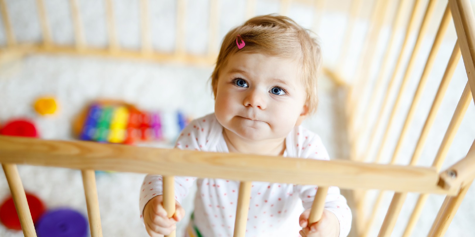 Beautiful little baby girl standing inside playpen.