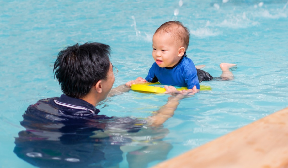 Happy infant enjoying his first swim in pool with his dad