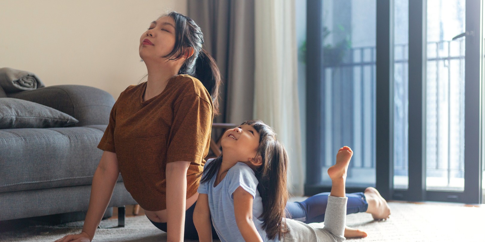 cute daughter practicing yoga with mother in the living room of apartment