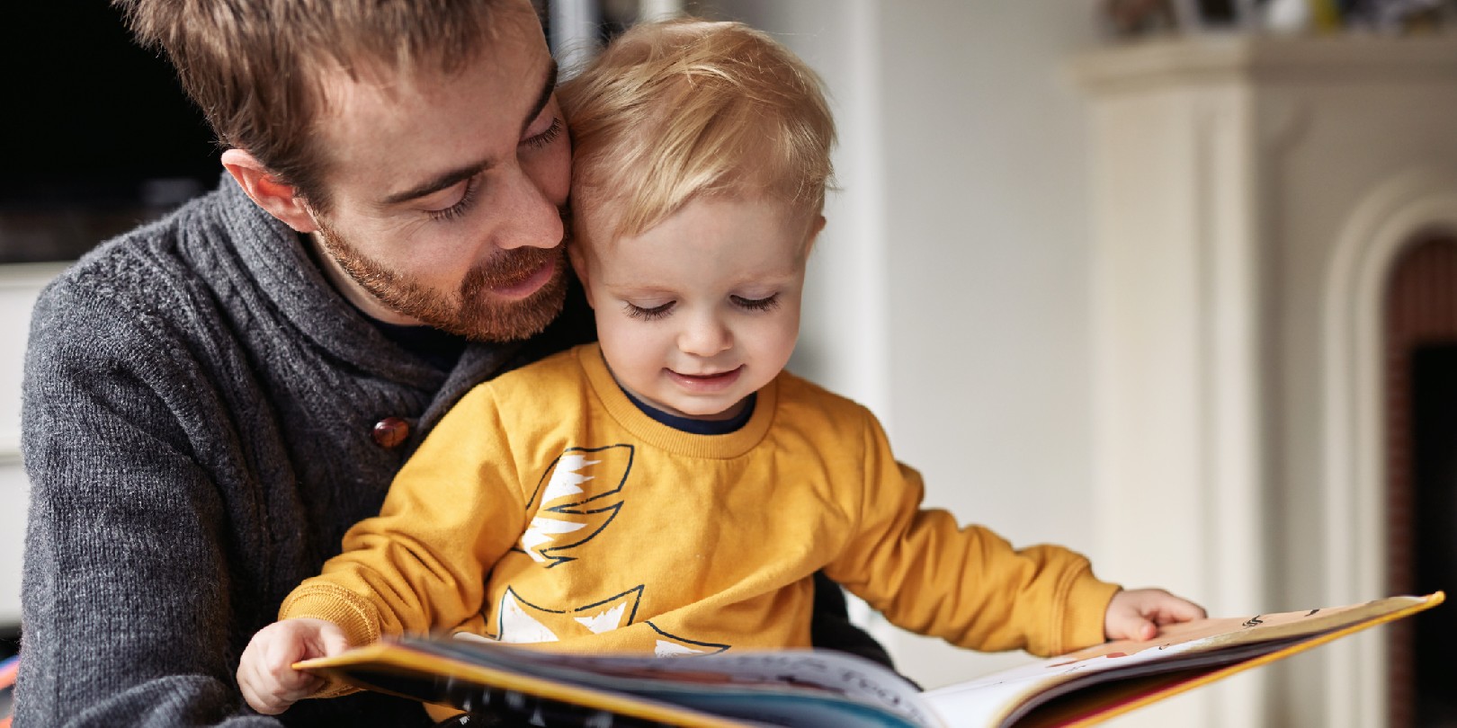 Cropped shot of an adorable little boy reading a book while sitting with his father at home