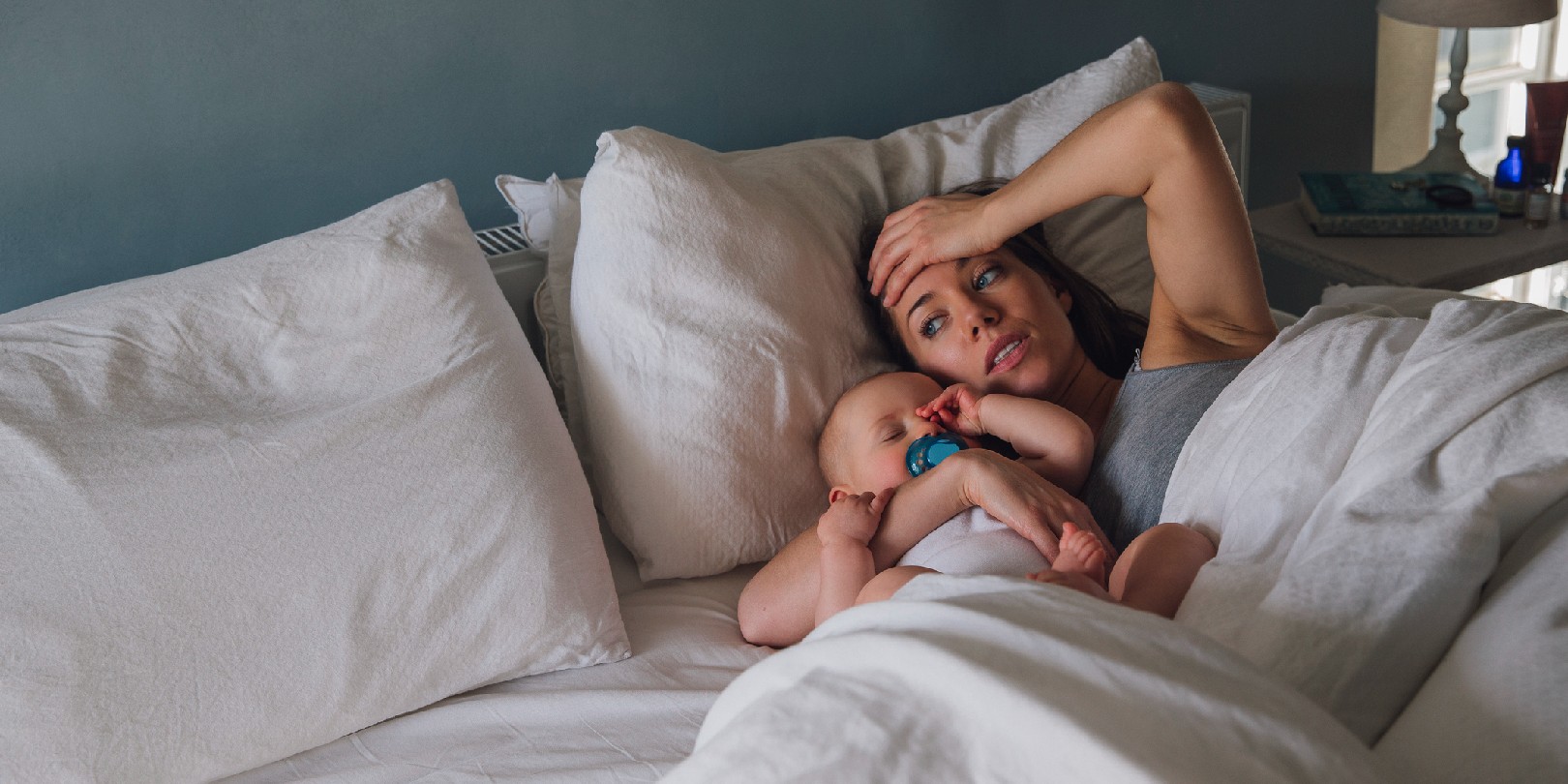 surviving-the-18-month-sleep-regression mighty-moms Young mother is lying in her bed with her baby daughter asleep in her arms