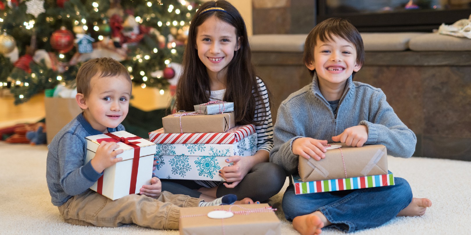 Three cute young ethnic siblings smile at the camera in a cozy holiday living room.