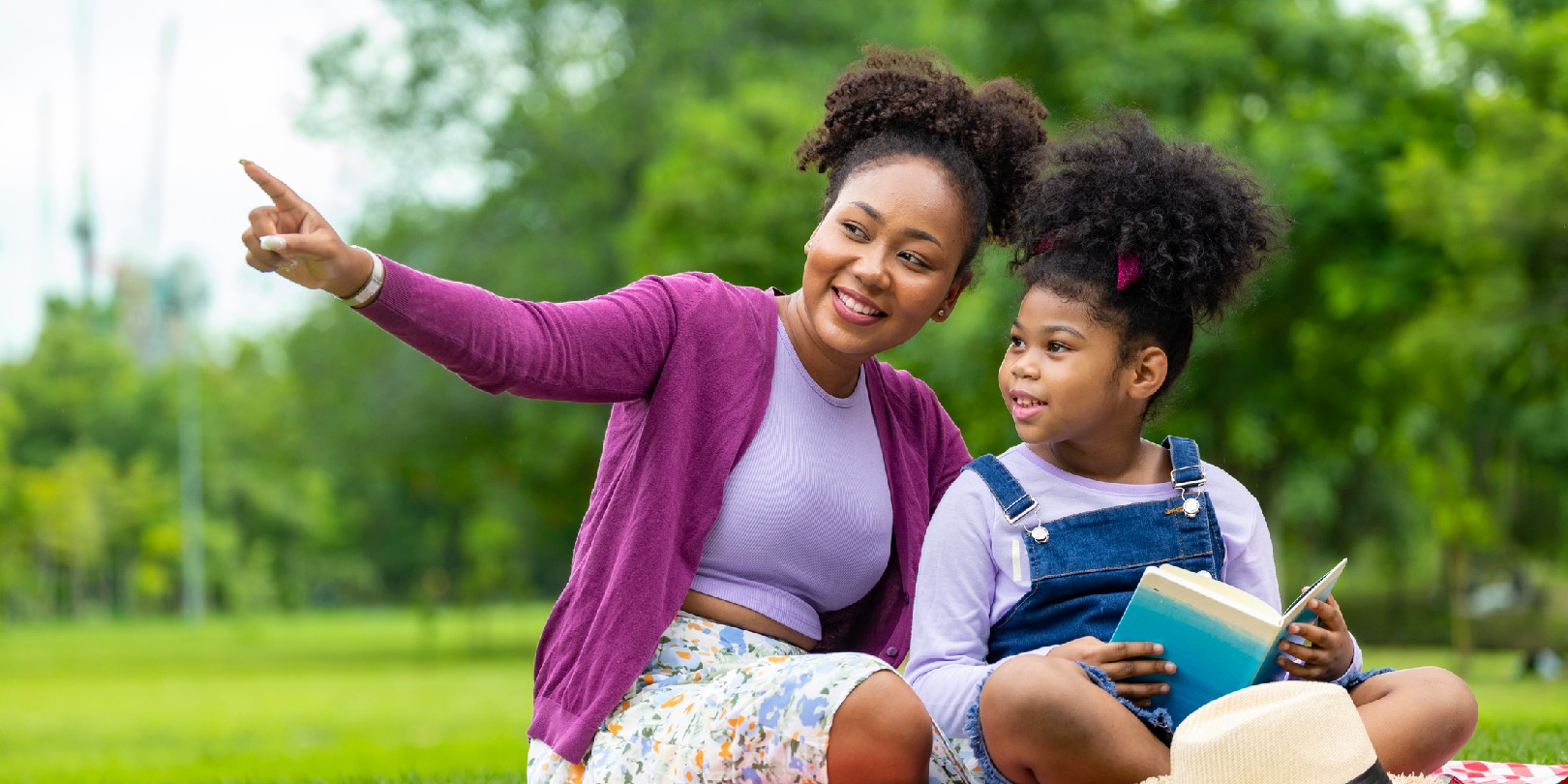 African American teacher is teaching her young student to read while having a summer outdoor class in the public park for education and happiness