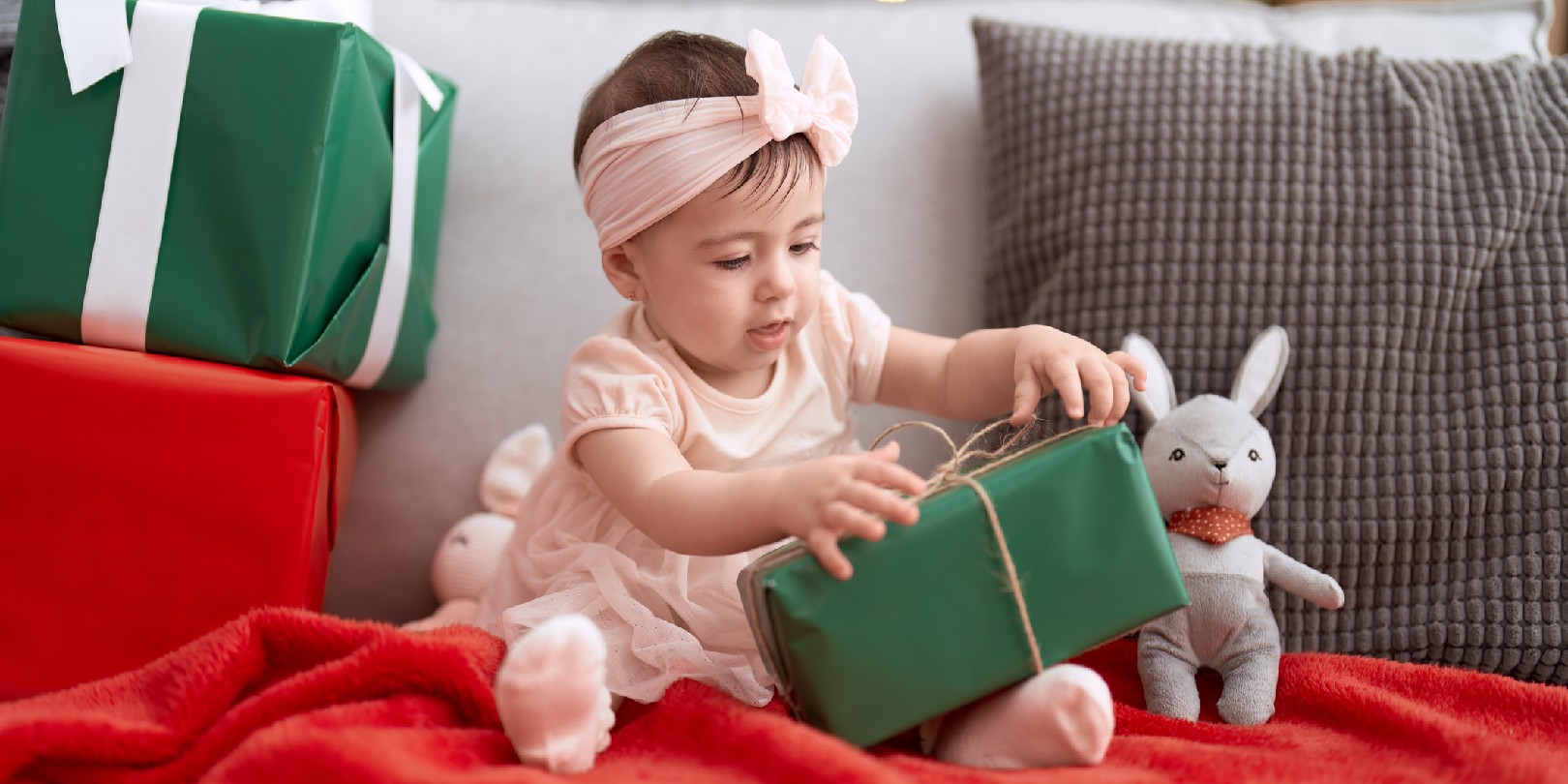 Adorable toddler opening christmas gift sitting on sofa at home