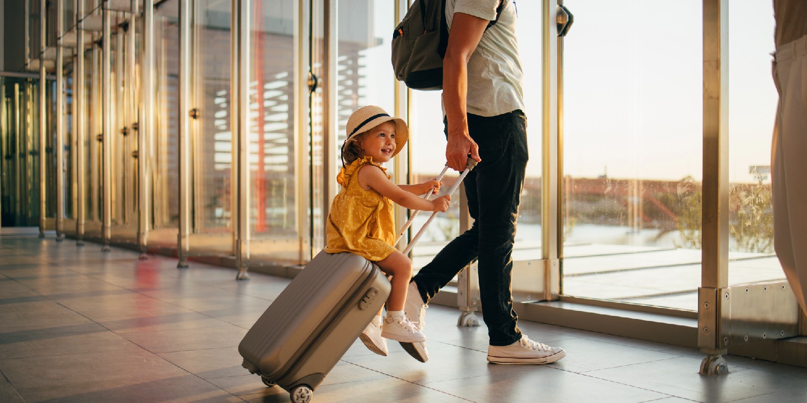 Cheerful husband and his anonymous wife walking with their little girl sitting on luggage at the airport