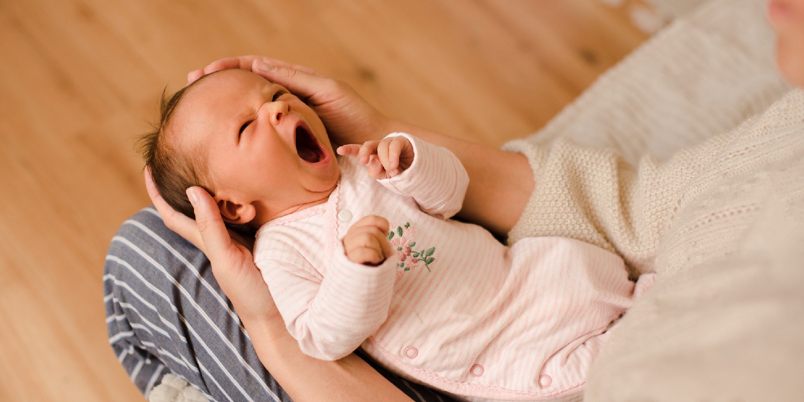 Cute infant baby girl yawning and wake up on mother hands in room at home close up top view. Motherhood. Little newborn crying with colic pain