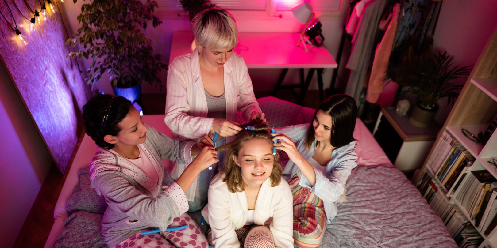 High-angle view of young Caucasian women styling a friend's hair and having fun at a slumber party.