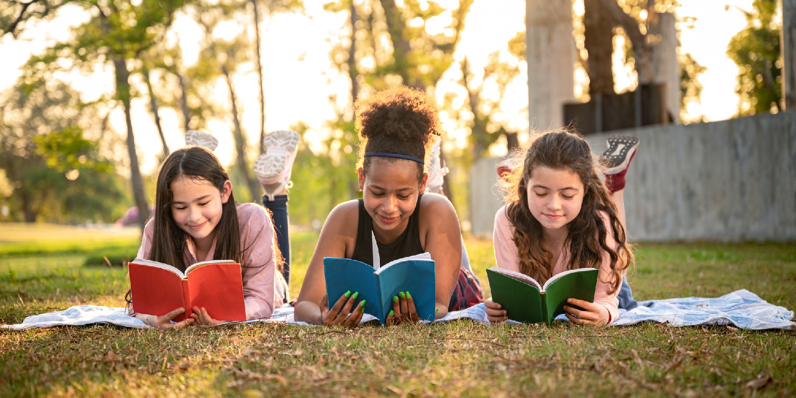 summer-reading-for-kids mighty-moms Student girl lie down reading book with sunset in the school park