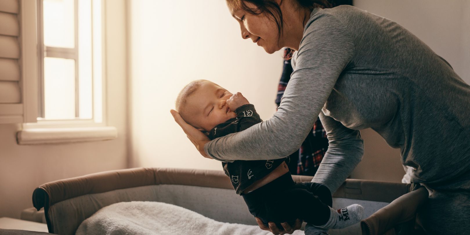 how-to-get-an-overtired-baby-to-sleep mighty-moms Mother Putting Her Baby to Sleep on a Bedside Baby Crib
