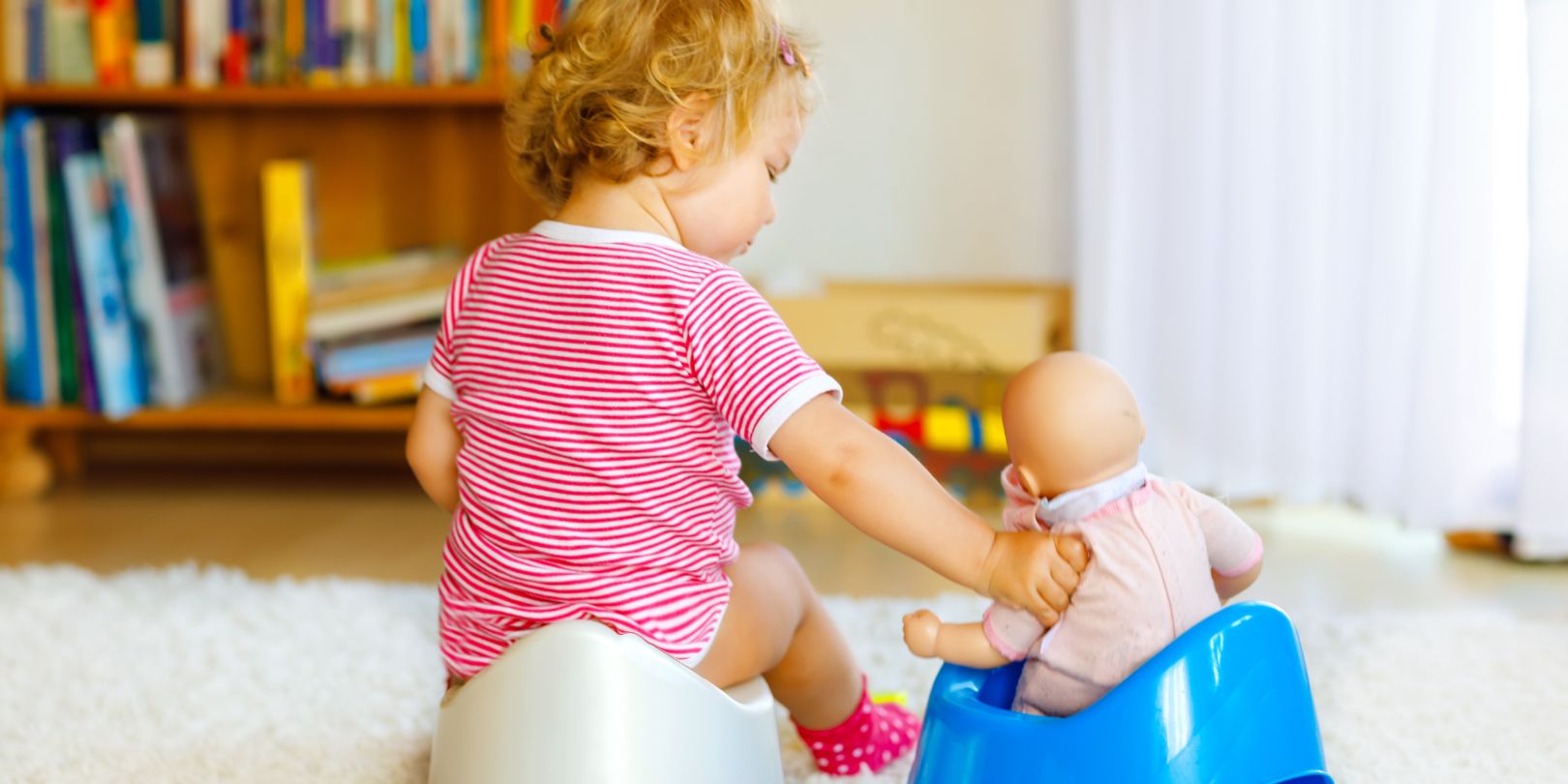 Close-up of cute little 12 months old toddler baby girl child sitting on potty. Kid playing with doll toy. Toilet training concept. Baby learning, development steps