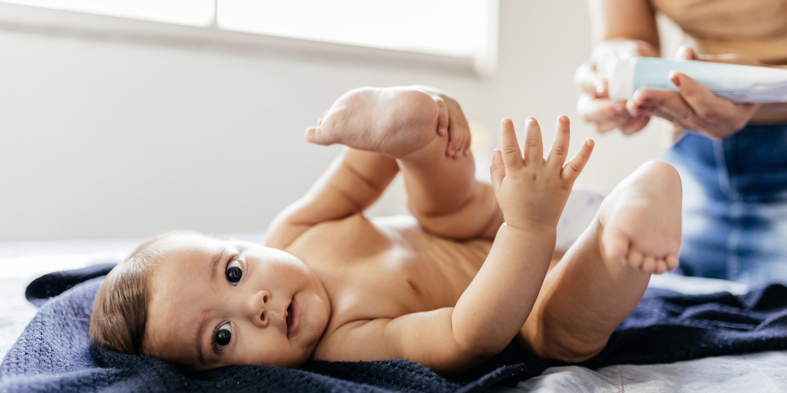 Mother changing baby's diaper in bed. Mother applies diaper rash cream.